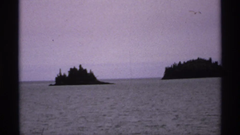 1971 Isle Royale home-movie view of low forested islands across rippled lake water with muted purple-blue exposure.