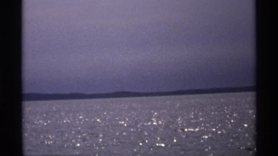 1971 Isle Royale view across rippling water toward a low distant shore, framed by dark vertical edges from the film scan.