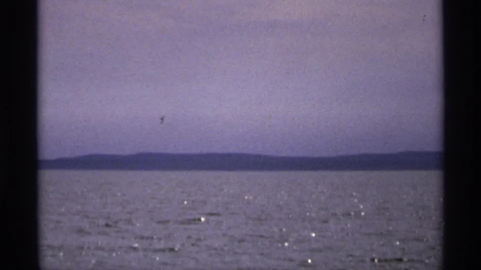 1971 Isle Royale home-movie frame showing open water, a hazy sky, and a distant low landmass across the horizon.