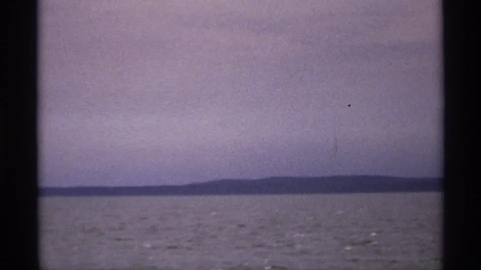 Wide 8mm Isle Royale water view with a dark distant shoreline, pale sky, and visible home-movie frame edges.