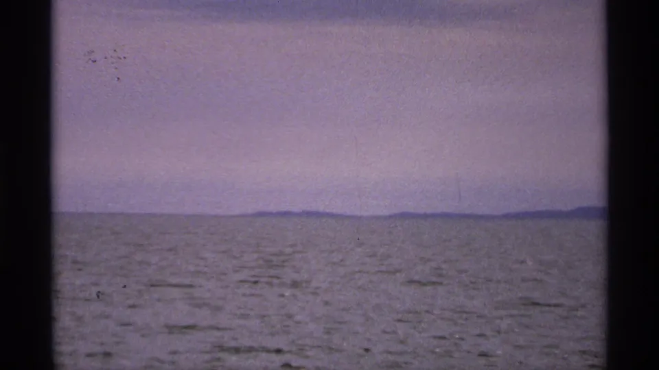 Muted 1971 Isle Royale water scene, showing a low horizon, pale sky, and small dust marks from the 8mm film scan.