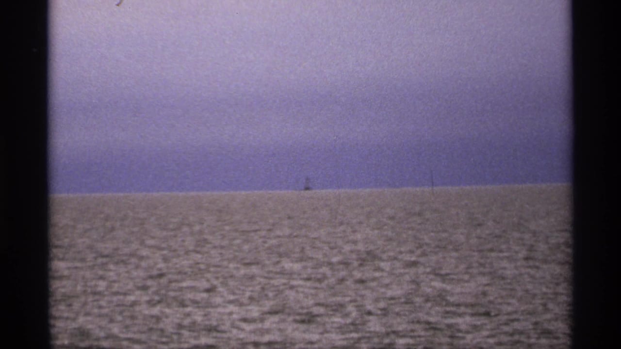 Open lake water under a muted sky with a tiny distant object near the horizon.