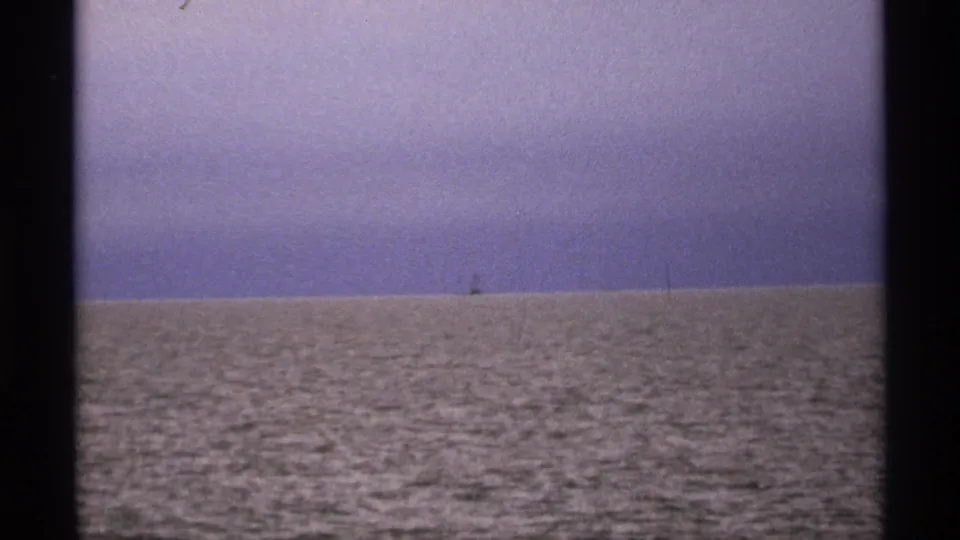 1971 8mm Isle Royale-area lake view with calm rippled water, purple-blue sky, and a small distant object on the horizon.