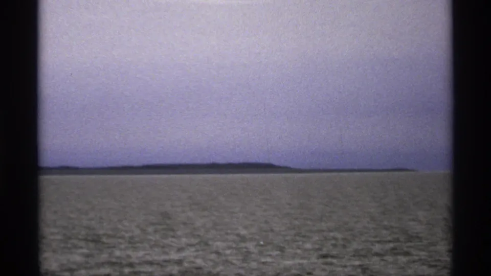 1971 8mm view of a low Isle Royale-area landmass across calm Great Lakes water, seen through soft home-movie grain.
