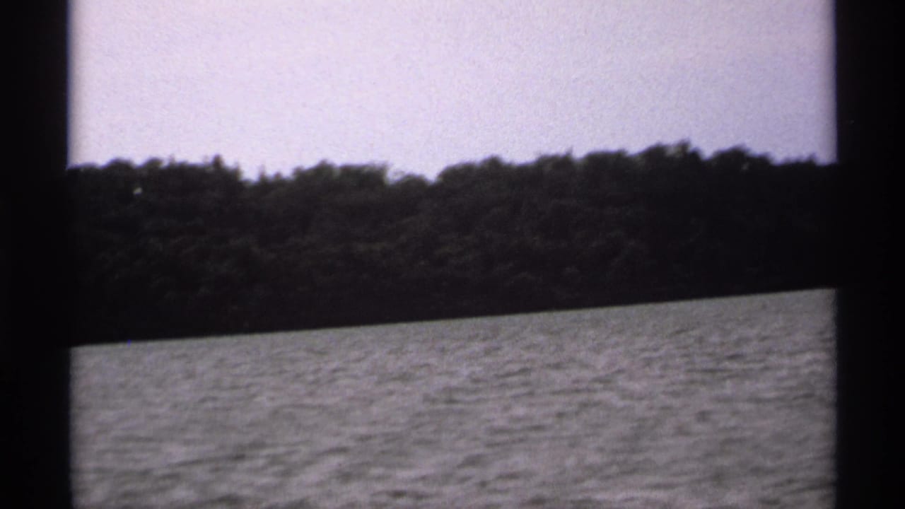 Rippling water below a dark wooded island shoreline and pale sky, seen through heavy film frame borders.