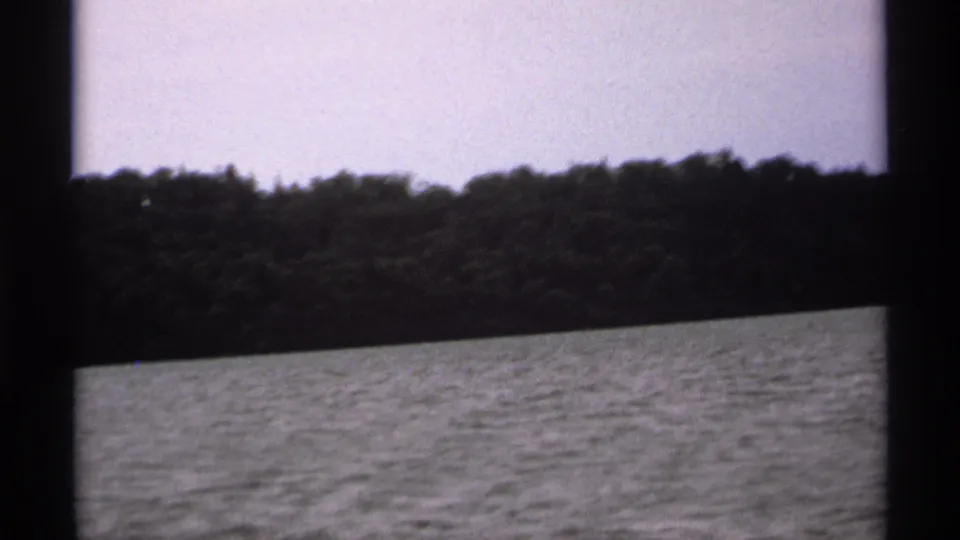 1971 8mm view near Isle Royale, Michigan, showing open water, a wooded shoreline, and pale sky from a moving boat.