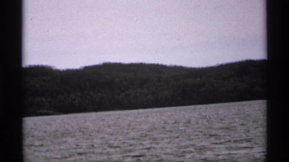 1971 Isle Royale 8mm view of rippled lake water below a dark wooded shore and softly exposed sky.
