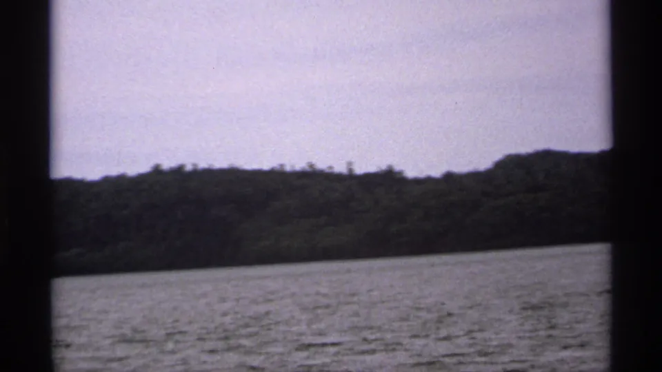 1971 Isle Royale home-movie frame showing open lake water and a low wooded horizon from a boat-travel perspective.