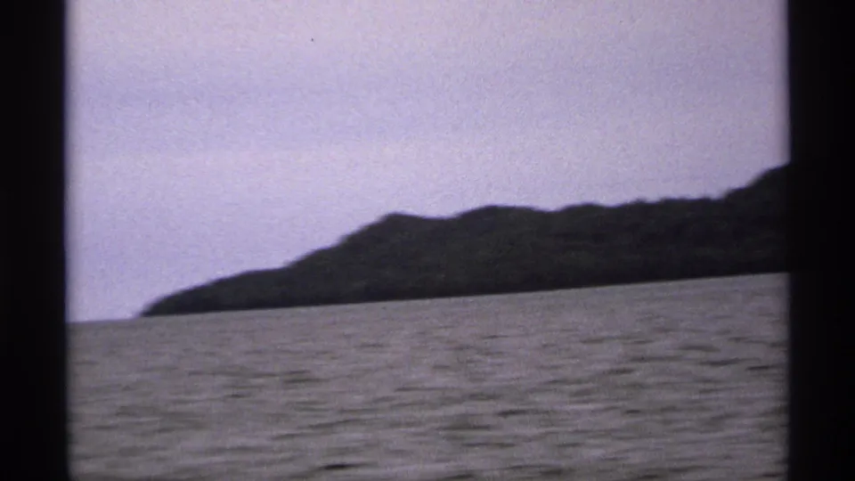 A low wooded Isle Royale shoreline runs along the waterline in this 1971 8mm passenger view over the lake.