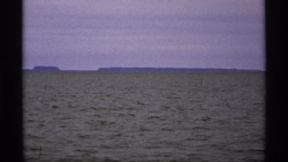 Distant low islands sit on the Isle Royale horizon beyond open Great Lakes water in grainy 1971 8mm footage.