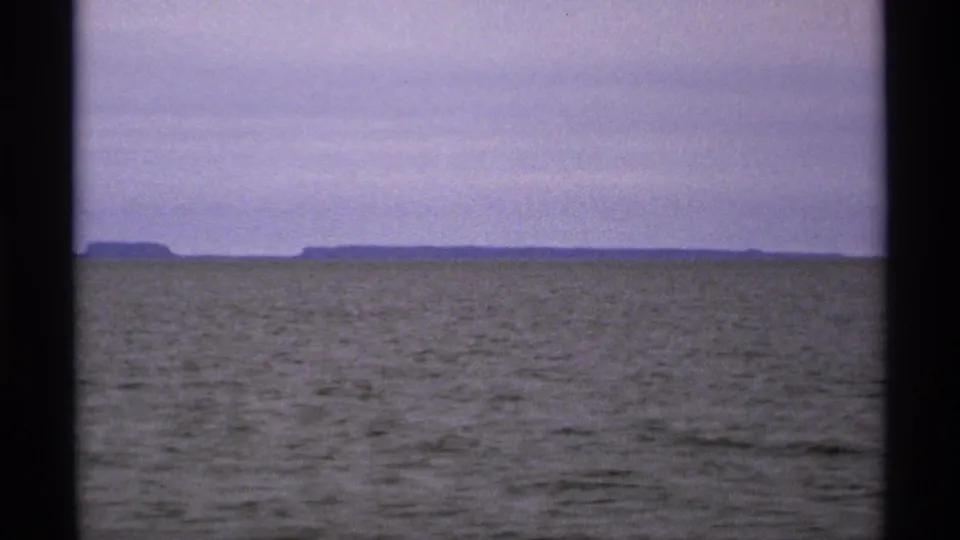 1971 Isle Royale home-movie frame showing open Great Lakes water, a pale sky, and a low shoreline in the distance.