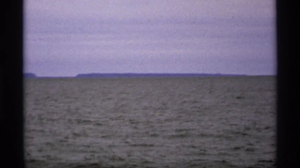 Isle Royale 8mm frame from 1971 with textured lake water, a low horizon, and distant land beneath a subdued sky.