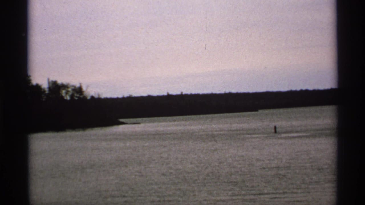 Calm water with a distant tree-lined shore seen through dark film gate edges.
