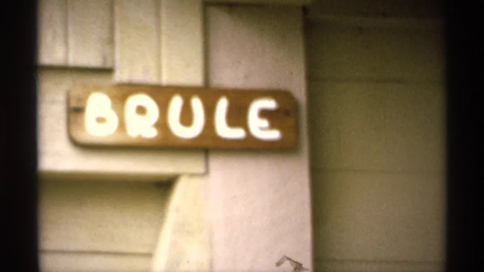 Close 1971 Isle Royale view of a hand-painted BRULE sign on a wooden cabin exterior with soft 8mm focus.