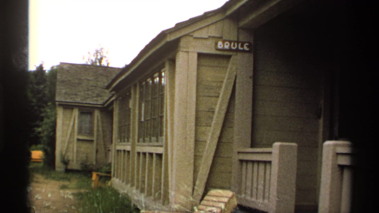 Rustic wooden cabin with BRULE sign beside a narrow path and trees.