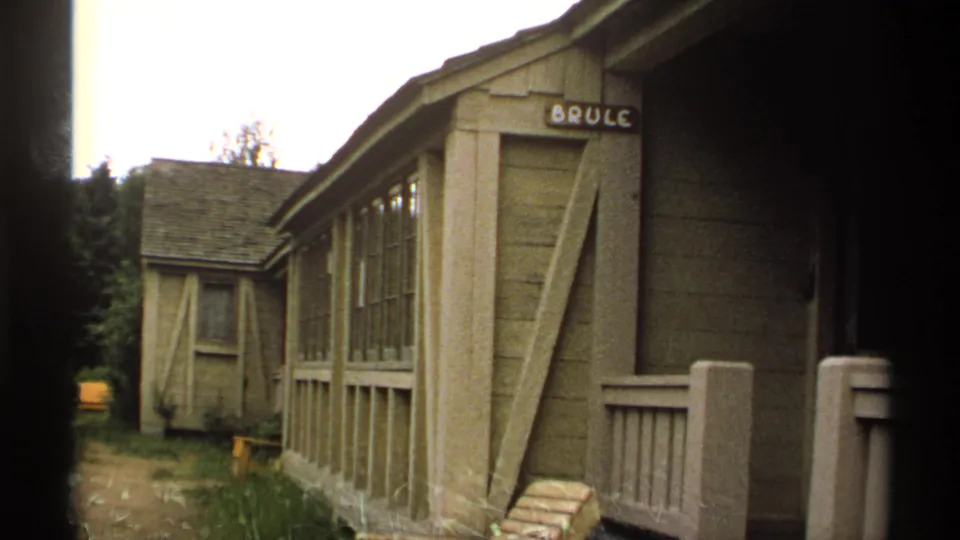 1971 Isle Royale 8mm frame showing a rustic wooden cabin marked BRULE, with screened windows, a porch railing, and wooded surroundings.