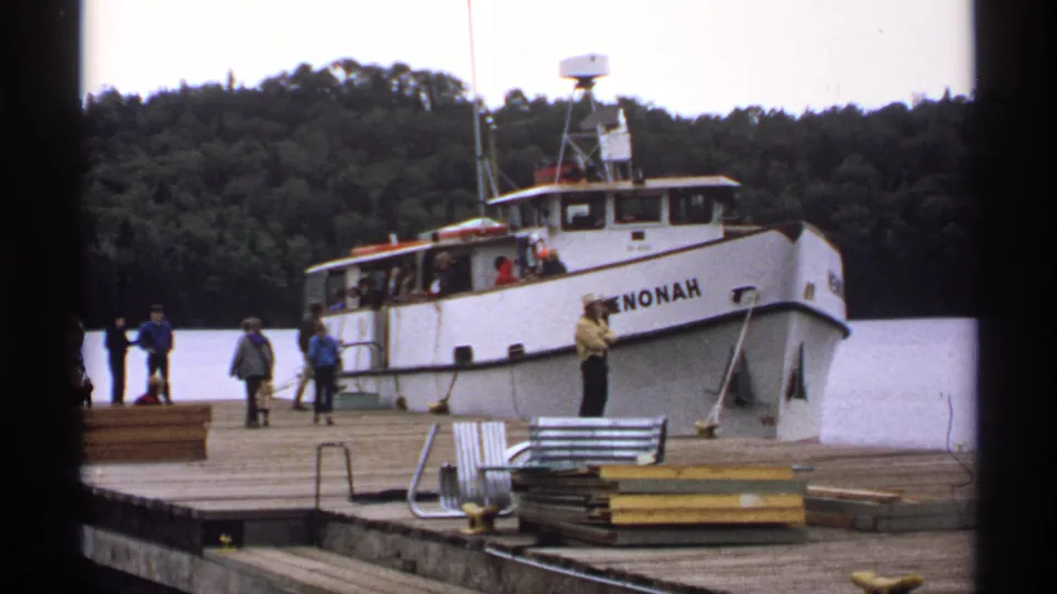 1971 Isle Royale frame showing the PENONAH moored at the pier as several passengers stand nearby, with stacked dock materials in the foreground.