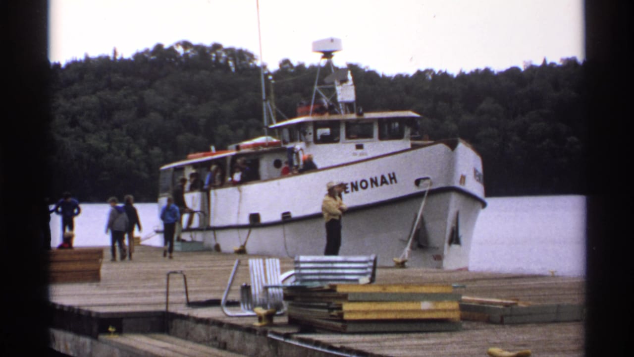 White boat docked at a wooden pier with several visitors nearby.