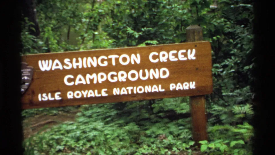 Wooden Washington Creek Campground sign for Isle Royale National Park filmed amid dense greenery in 1971.