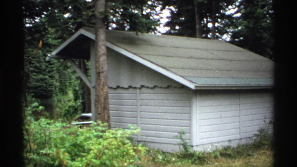 Small gray wooden utility building or cabin in a wooded Isle Royale campground setting, filmed in 1971.