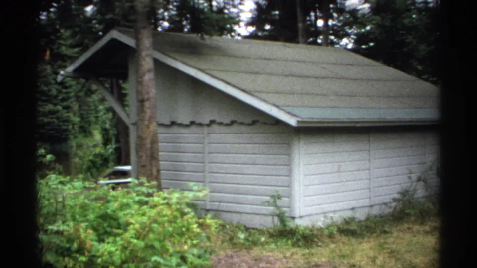 1971 Isle Royale frame showing the pale wooden structure more tightly, with dense vegetation and tall trees around it.