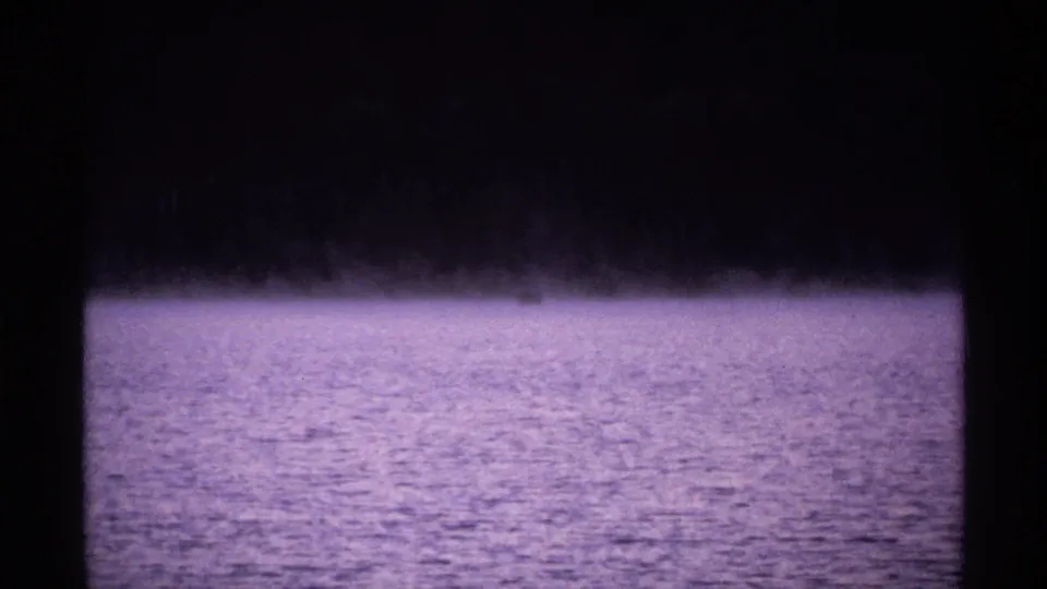 1971 Isle Royale home-movie frame showing fog or low mist over a purple-toned lake with a dark distant shoreline.