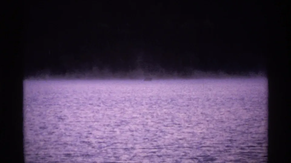 1971 Isle Royale 8mm frame of a fog-covered lake surface and faint dark shoreline, tinted purple by the film scan.