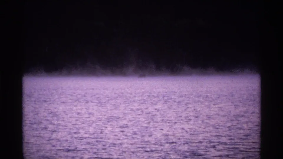 1971 Isle Royale 8mm frame showing calm lake water under mist with a dark distant shoreline and visible film gate edges.