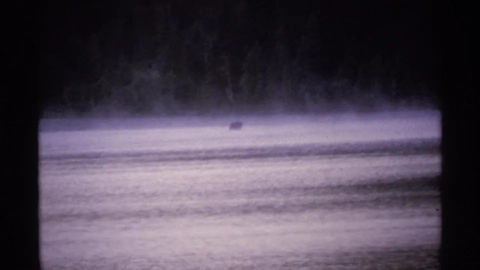 1971 Isle Royale home-movie frame showing rippled lake water, surface mist, and a small dark object near the far shore.