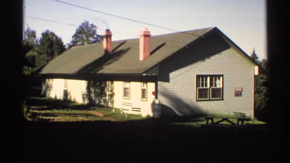 The 1971 8mm footage shows a closer exterior view of the wooden house, its roofline, brick chimneys, windows, lawn, and surrounding trees.