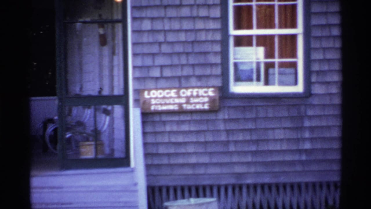 Close view of a shingled building with a lodge office and souvenir shop sign near a screen door.