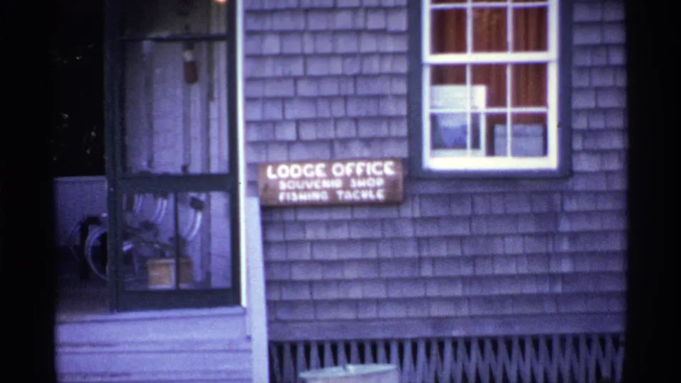 Isle Royale lodge exterior in 1971 with a readable lodge office, souvenir shop, and fishing tackle sign on a weathered shingled wall.