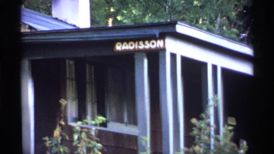 1971 Isle Royale frame showing the Radisson sign over a shaded porch with white posts and surrounding greenery.