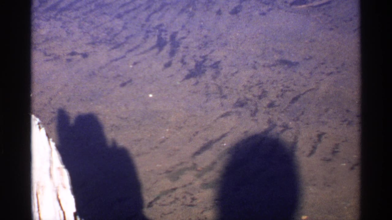 Human shadows fall across rough ground beside a pale vertical edge.