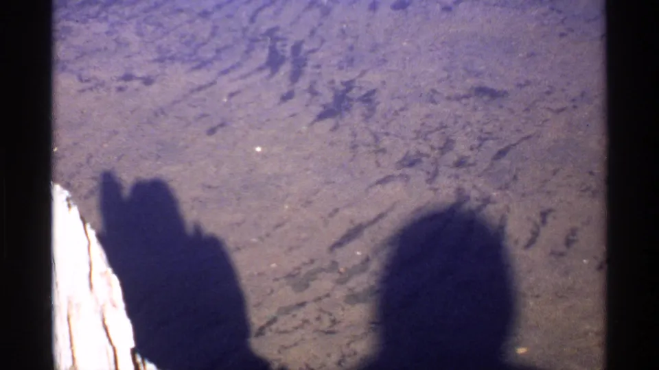 1971 Isle Royale frame with human shadows cast across textured ground, likely filmed from a shaded outdoor position.