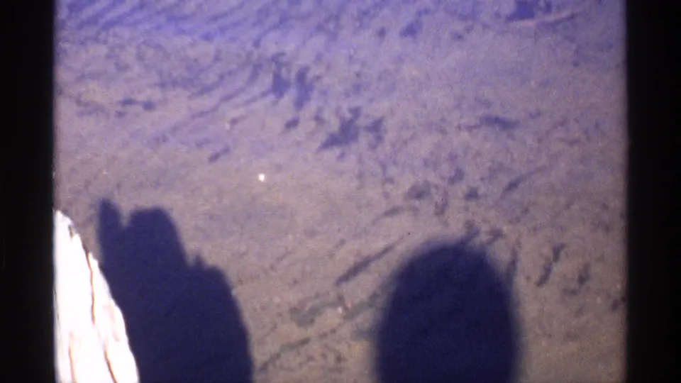 1971 Isle Royale home-movie still showing shadowed figures on the ground before the view shifts toward foliage.