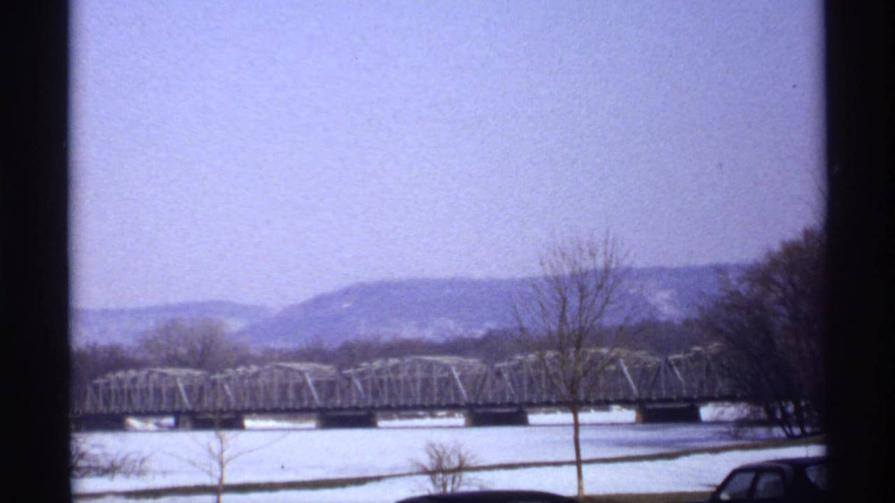 Wide 1971 La Crosse, Wisconsin winter view showing a metal truss bridge across a snowy or frozen river with bare trees and distant bluffs.