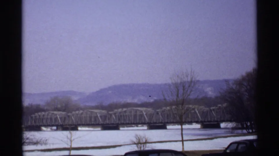 La Crosse, Wisconsin winter riverfront view from 1971, with a long metal bridge, snow cover, leafless trees, and low hills beyond the river.