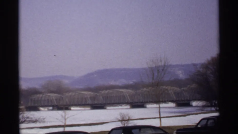 1971 La Crosse footage frames the truss bridge and snow-covered riverfront against muted hills under a pale winter sky.