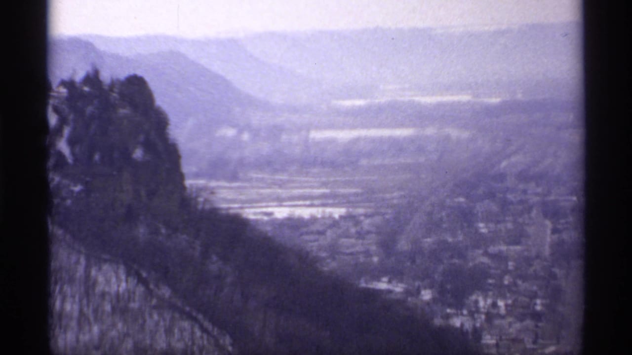 High view over wooded hillside toward a hazy river valley and distant bluffs.