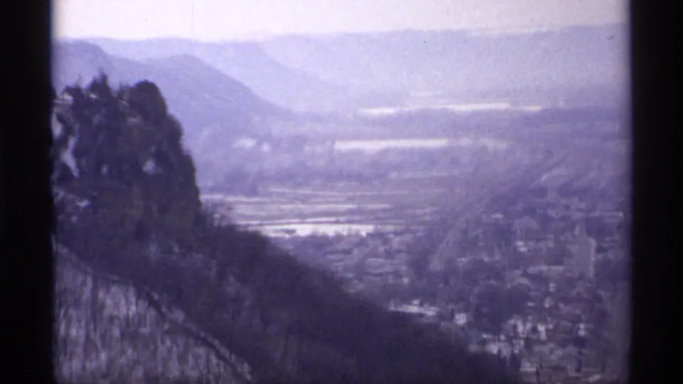 1971 La Crosse-area high vantage view with dark trees at left, snow-bright lowlands, haze, and distant hills on 8mm film.