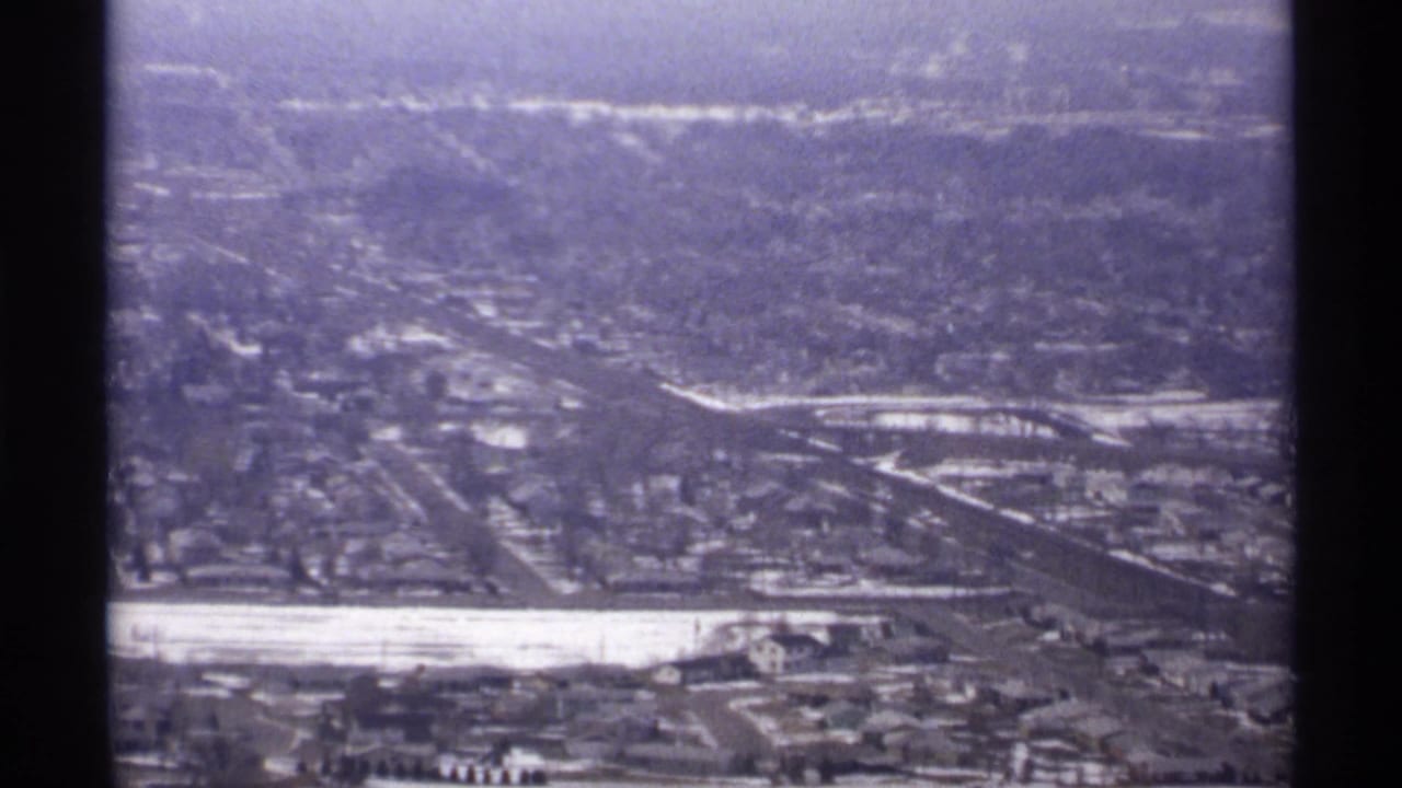 Elevated view of a city grid, roads, pale river area, and distant hills.