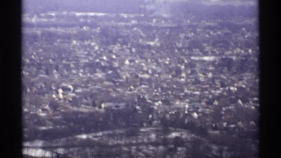 High-vantage 1971 La Crosse view showing dense rooftops, bare trees, snow traces, and a hazy hillside horizon on 8mm film.