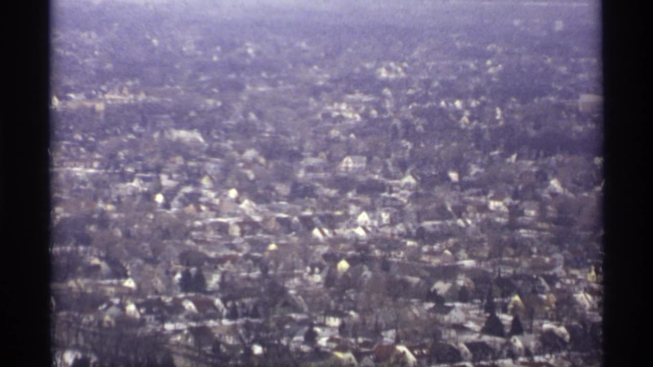 Aerial neighborhood view with many houses, bare trees, and pale winter roofs.