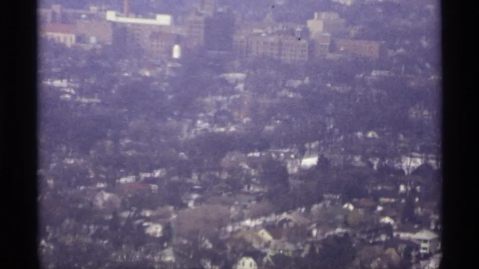 La Crosse aerial frame from 1971 showing rooftops, tree-lined residential blocks, and larger distant buildings in a hazy 8mm view.