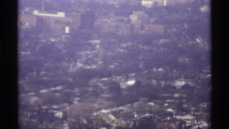 1971 La Crosse aerial frame showing hazy residential blocks, roads, trees, and distant larger buildings on 8mm film.