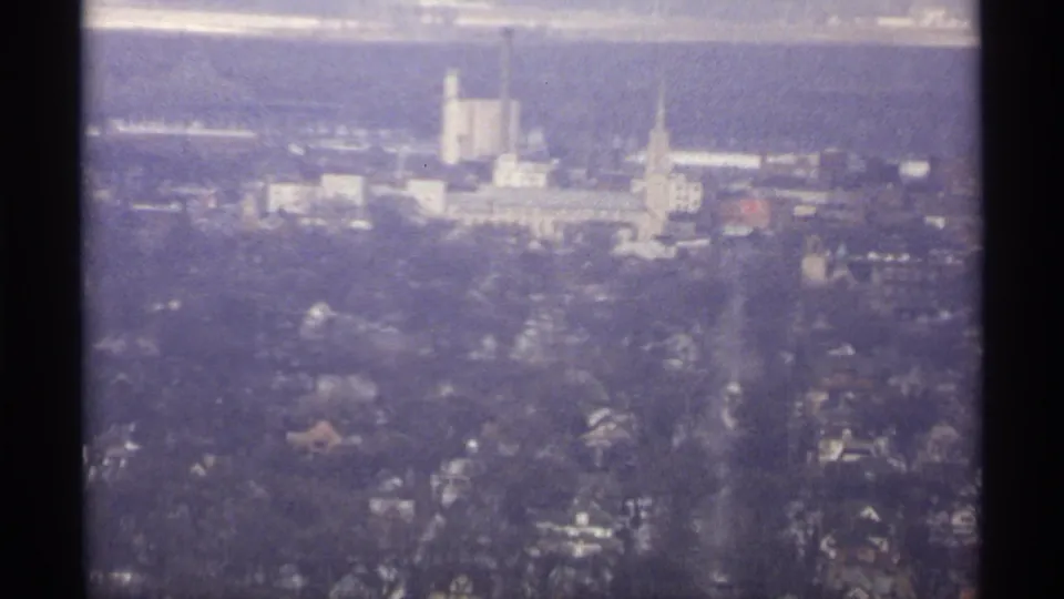 1971 La Crosse aerial frame with residential areas, roads, a steeple-like tower, and larger light-colored buildings under hazy light.