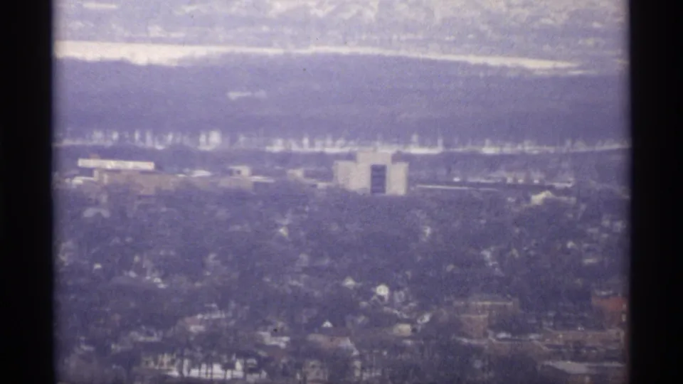 1971 La Crosse winter aerial showing a light-colored building, snowy rooftops, and water beyond the city.