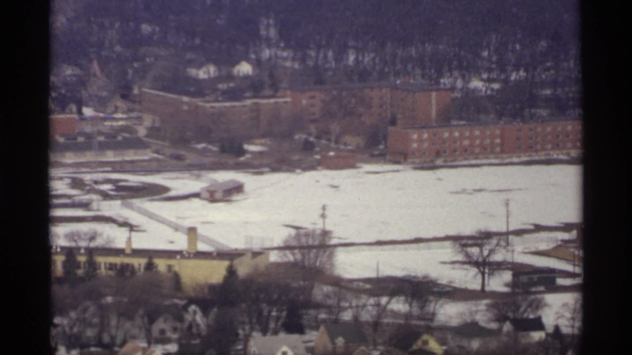 Snow-covered town view with brick buildings, bare trees, and distant hillside.