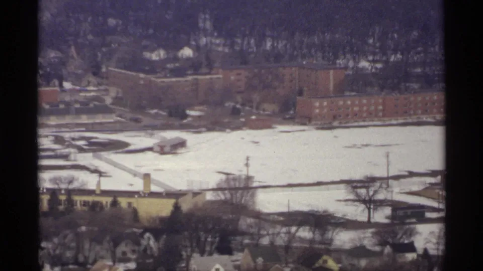 1971 La Crosse, Wisconsin overlook showing brick buildings, snowy open ground, bare trees, and a wooded hillside in soft 8mm color.